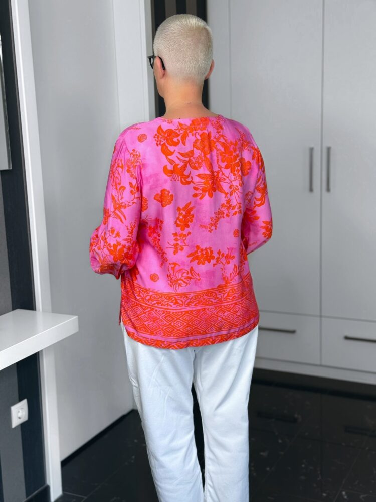 Person in pink Bluse und weißer Hose, Rückansicht