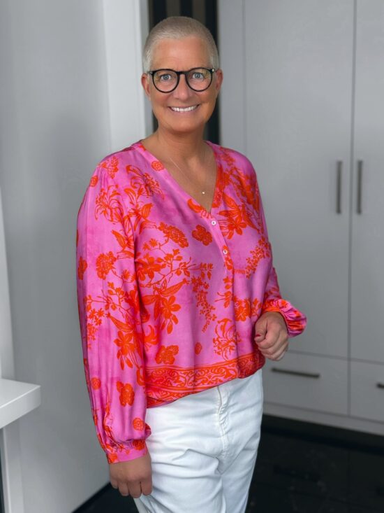 Frau mit Brille, pinke Bluse, kurze Haare, lächelnd.
