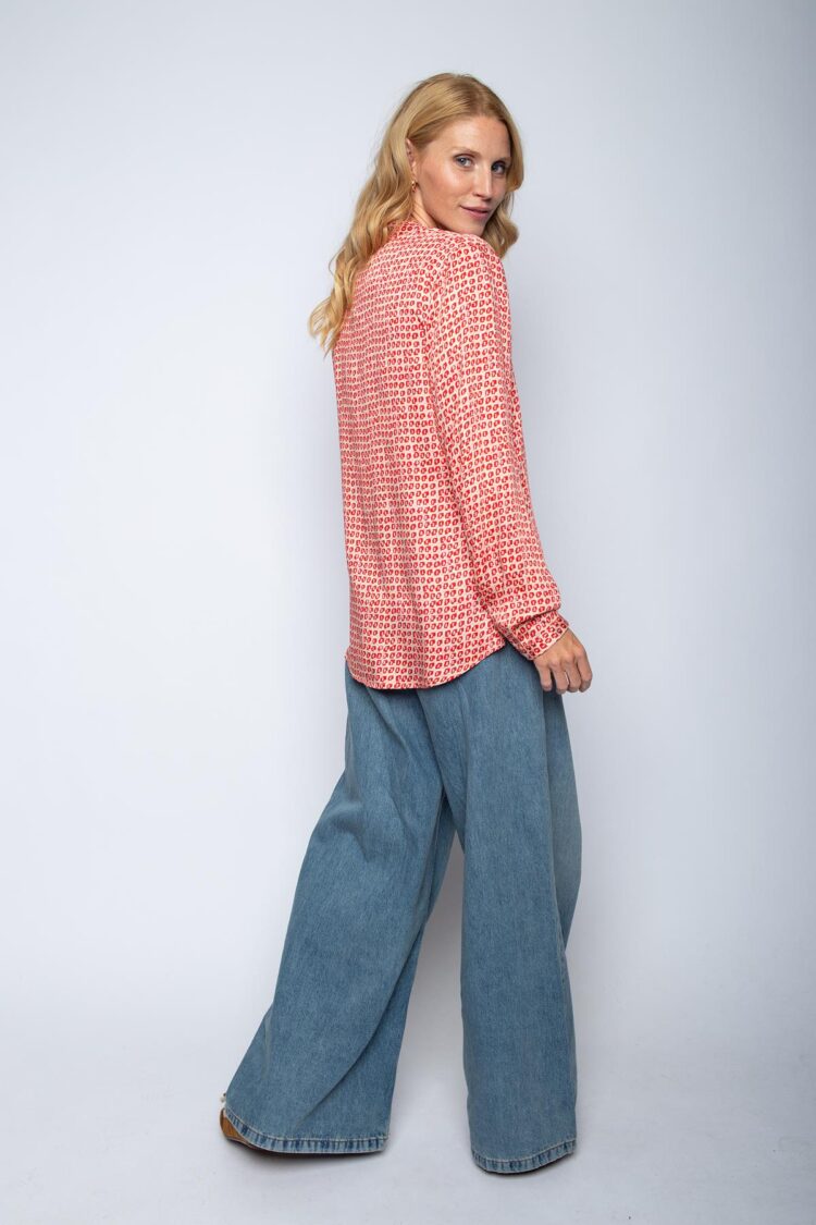 Frau im gemusterten Hemd und Jeans, zur Seite blickend.