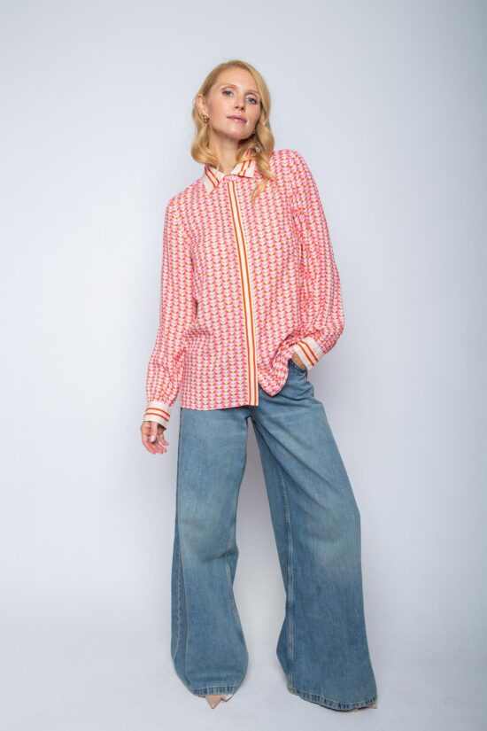 Frau in bunter Bluse und Jeans posiert.