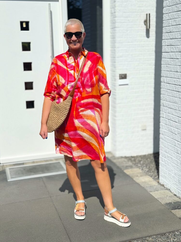 Frau mit buntem Kleid vor weißem Gebäude.