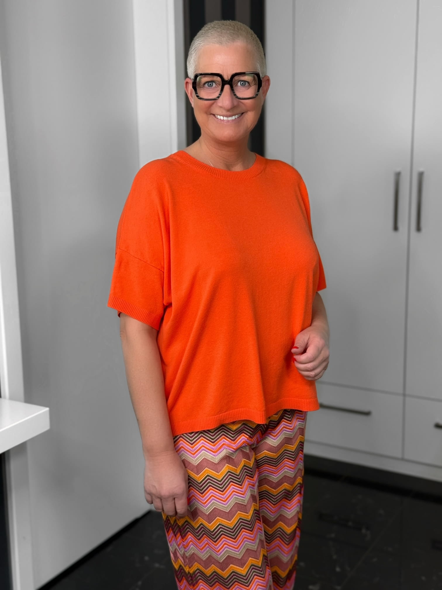 Milano Italy-Pulli-62-5268-9046-300-2 Lächelnde Person mit orangefarbenem Oberteil und Brille