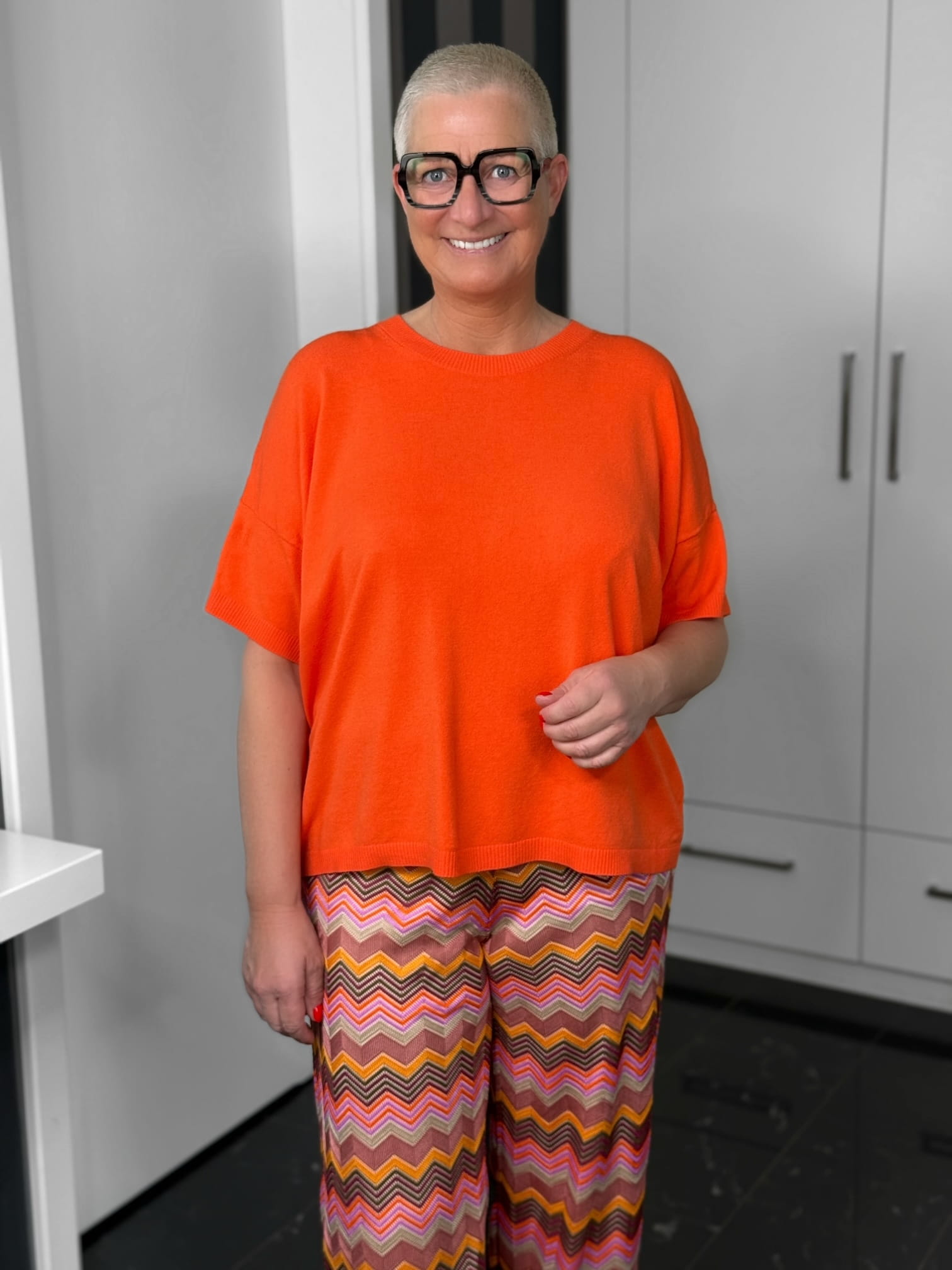 Milano Italy-Pulli-62-5268-9046-300-3 Lächelnde Person mit orangefarbenem Oberteil und Musterhose