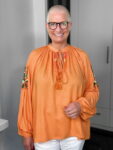 Lächelnde Person mit Brille und orangefarbener Bluse