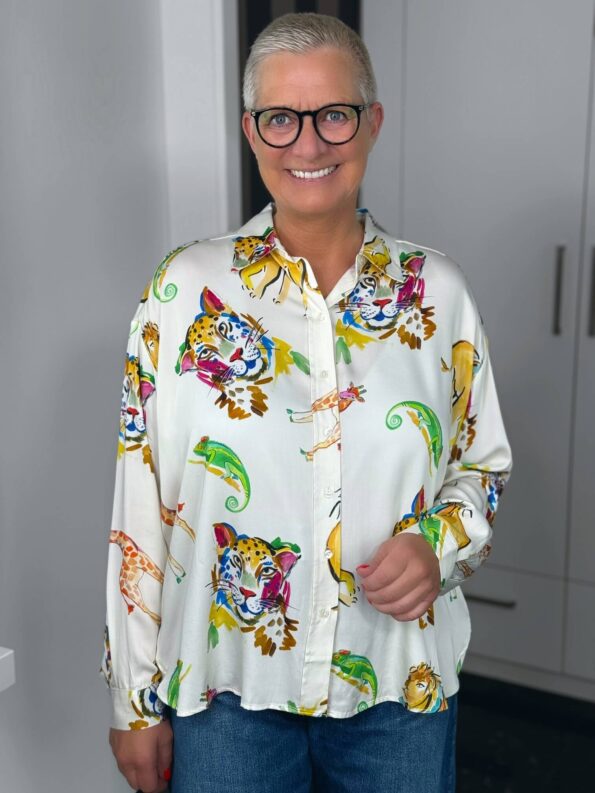 Lächelnde Frau mit bunter Tierprint-Bluse und Brille